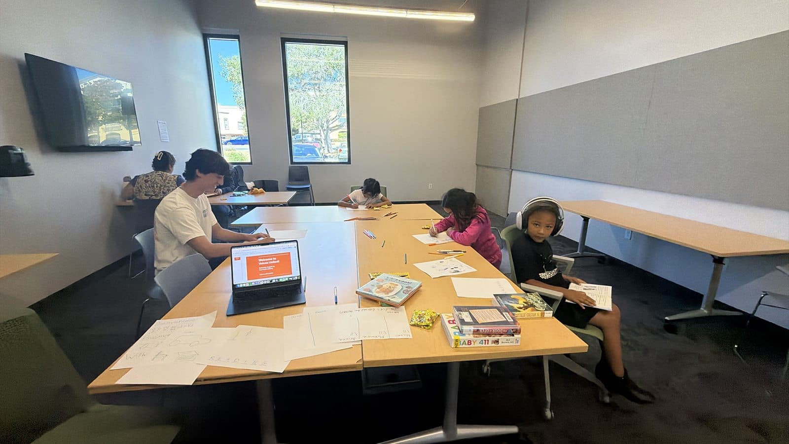 A welcoming classroom with children working on English-learning activities around shared tables.
