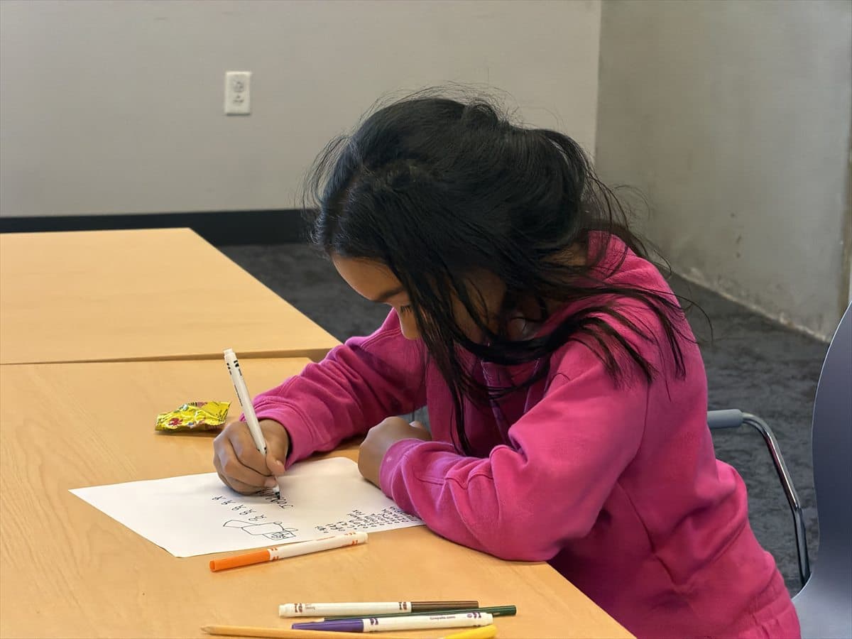 A child concentrating on a writing activity with colorful markers nearby.
